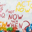 Graffiti on a white wall that says "If not us then who, if not now, then when?"