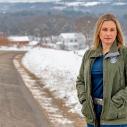 A woman stands by a wintery rural road