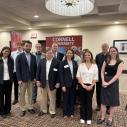 group of individuals standing and smiling in front of Cornell University sign