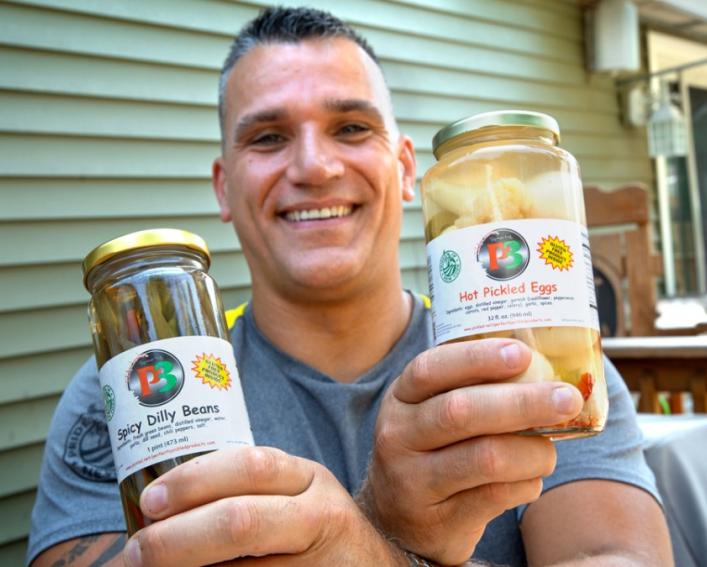 A man holding two jars of pickles 