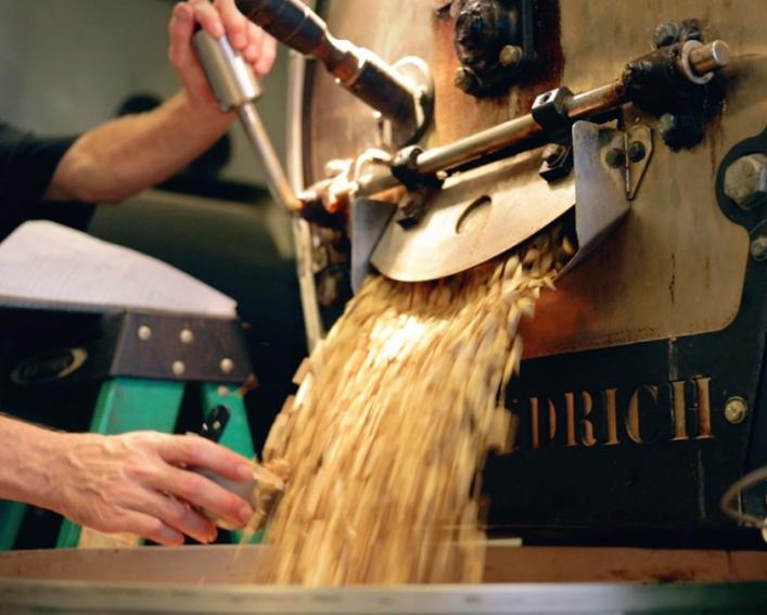 Tan colored seeds pouring out of the opening of a machine being operated by a man
