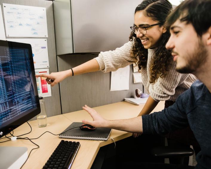 A young woman and a young man point at numbers on a computer screen