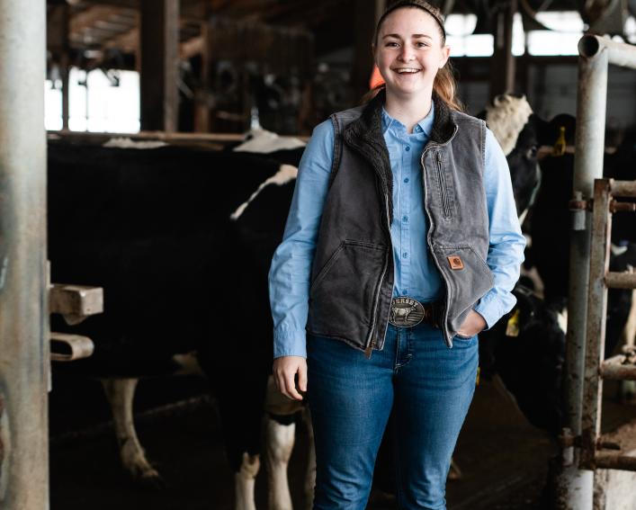 A female standing in front of a cow in a cow barn