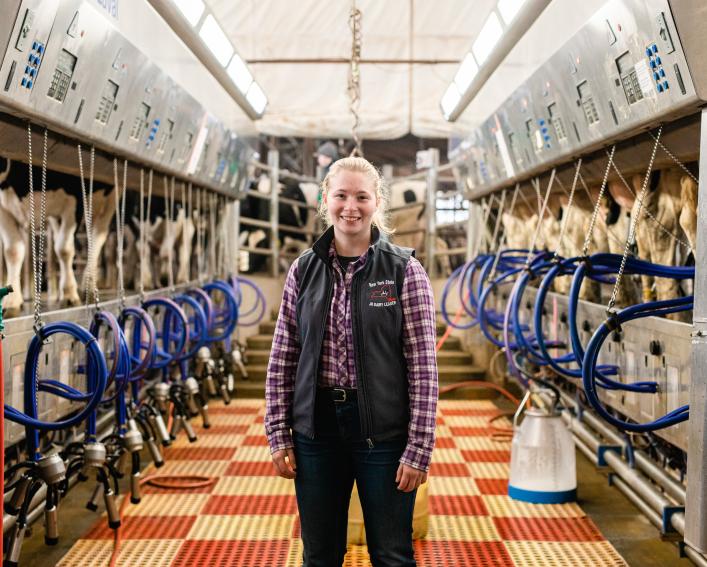 A young woman standing in a cow milking facility