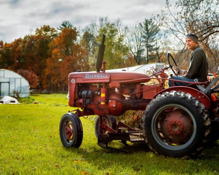 Farmer on small tractor in field with high tunnel in background