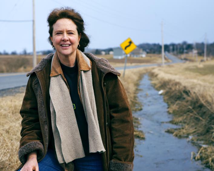 A woman stands next to a drainage ditch running along a rural highway