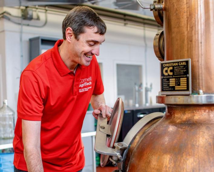 A man in a red shirt examines a copper distiller