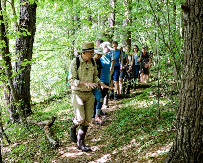 A man leads a group of college students along a wooded trail
