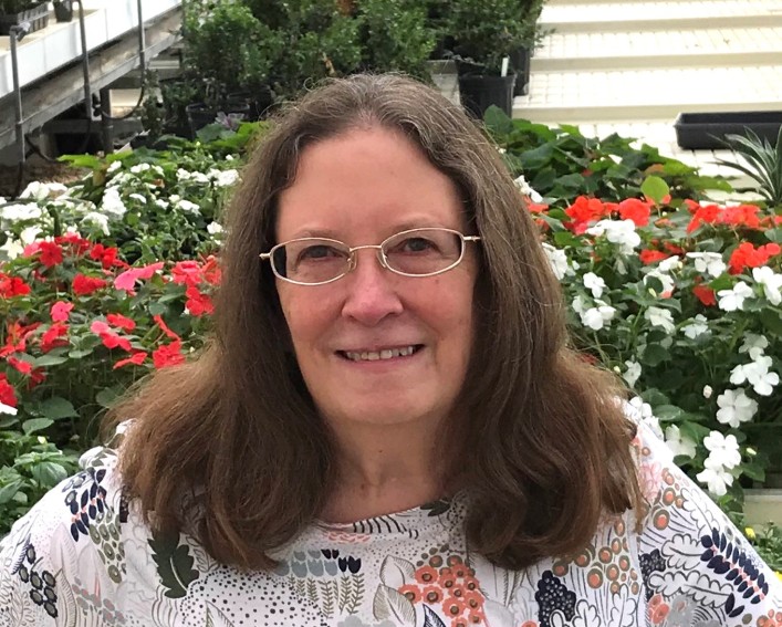 A headshot of a woman with glasses standing in front of flowers