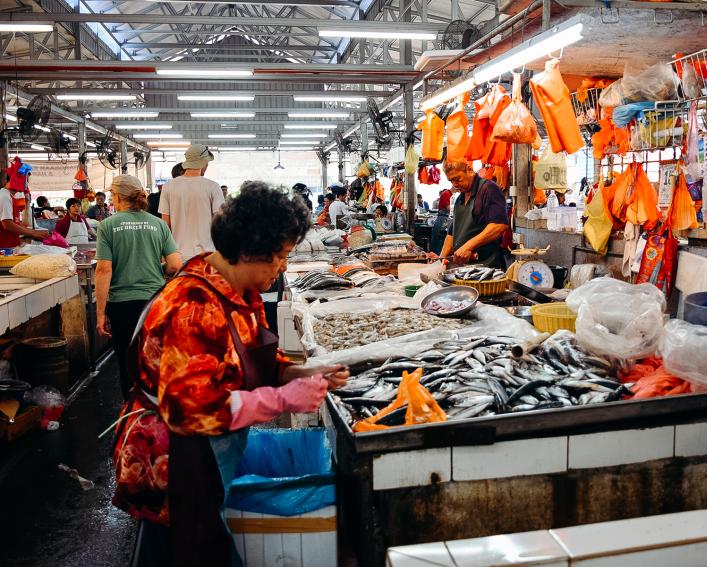 A woman stands in front of a container of fish at a Kuala Lumpur, Malaysia outdoor market.