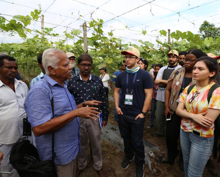 A man speaks to students standing in a field of crops