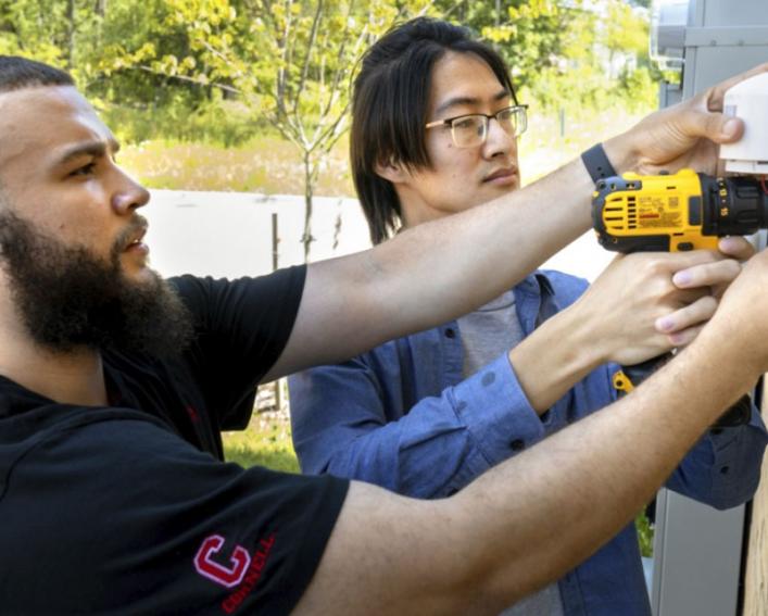 Two men drilling technology into the side of a house 