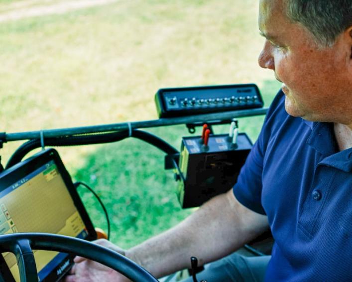 Terry Bates looks at computer while on his tractor