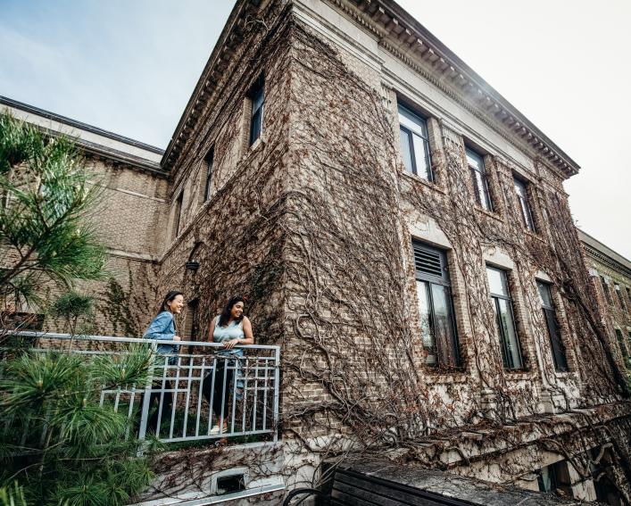 Two students on balcony with ivy-covered Plant Science building in background