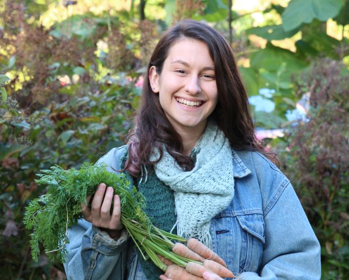 Emma standing and smiling while holding carrots. 