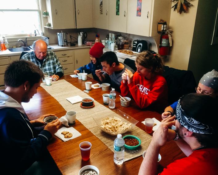 Students sit around a table eating lunch.