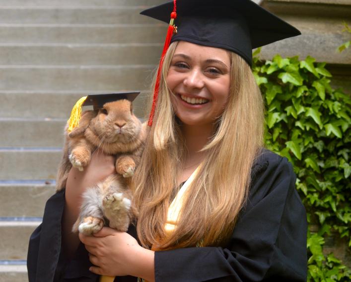 Erin Scannell standing in her graduation cap and gown holding Finn, her rabbit who is also wearing a graduation cap