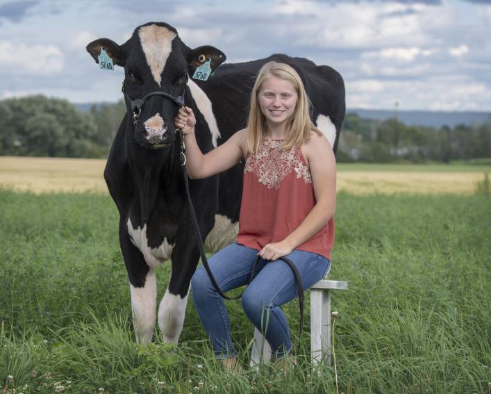 Rachel sitting on a stool outside holding onto a cow's bridal