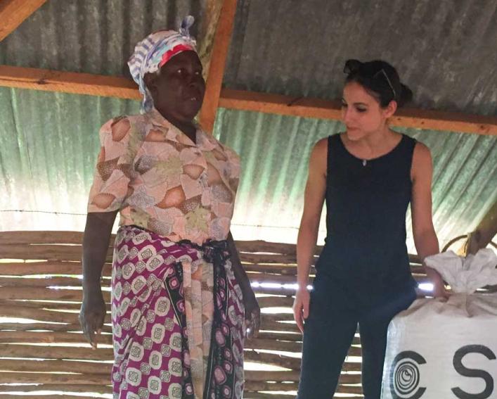 Two women stand inside a storage building next to a large bag of grain