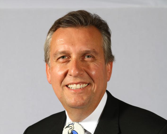 Portrait photo of man in a dark suit wearing a bolo tie.