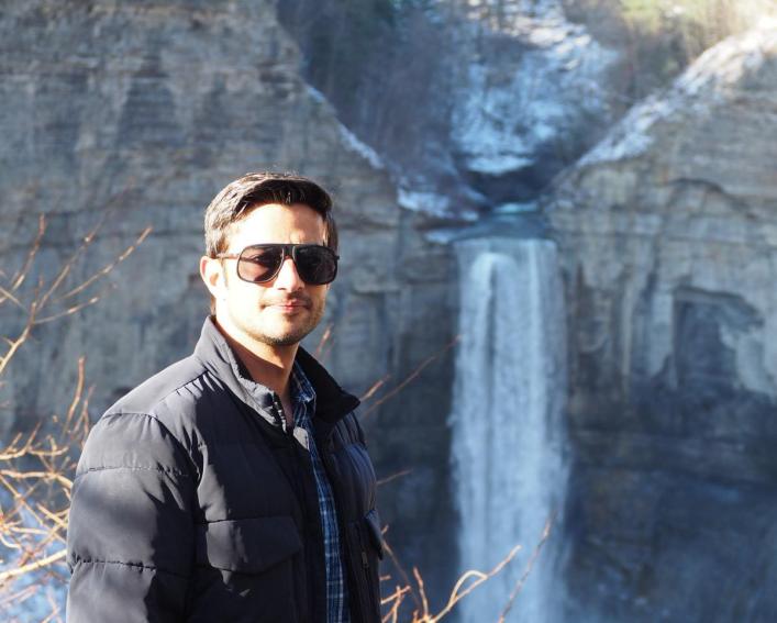Man poses for photo in front of a waterfall