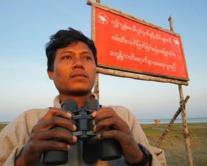 Man with binoculars in front of red sign