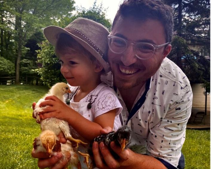 Pinny squatting with a child and holding baby chicks