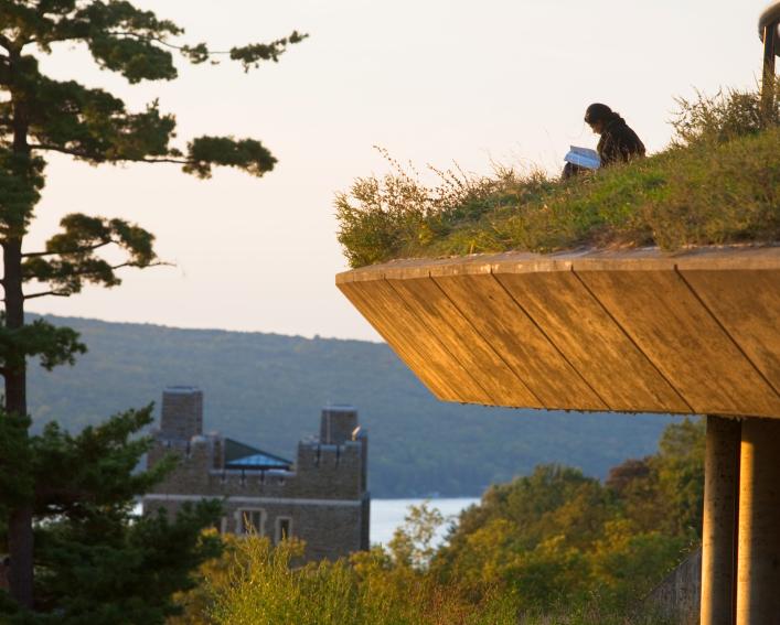 AIISP courses - Student sits on a grassy area reading a book, overlooking Cayuga Lake 