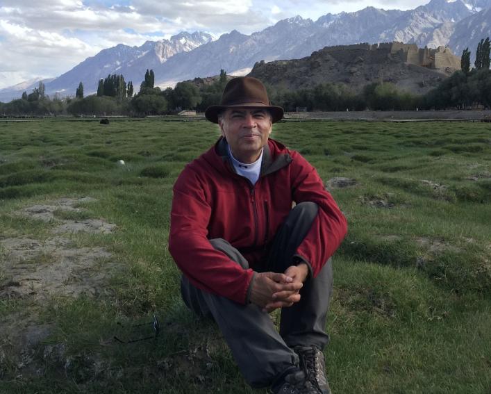 Photo of a man wearing a hat sitting in a view with mountains behind them.