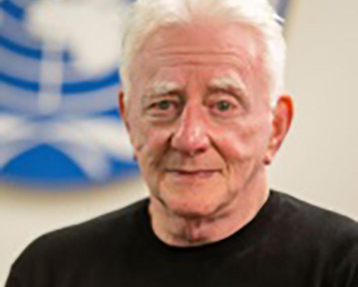 Headshot photograph of a man with white hair and a dark shirt.