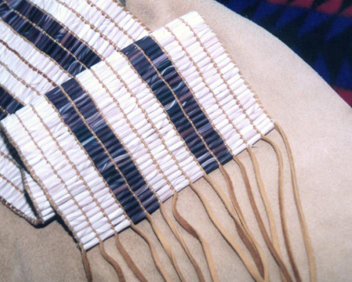 Photo of a beaded wampum belt consisting of three bands of white beads and two rows of purple beads.