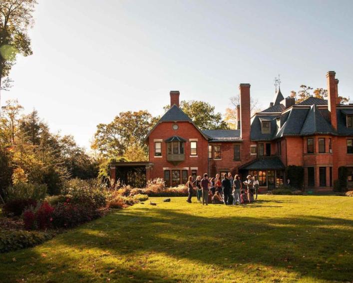 Photo of people at a cocktail hour in the backyard of a red brick house during the late afternoon light.