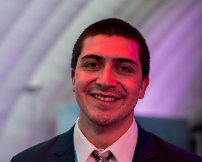 Headshot photograph of a man with short dark hair smiling wearing a suit and bolo tie.