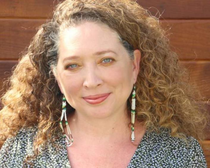 Headshot photograph of a woman with long curly blonde hair wearing beaded earrings and a light green shirt.