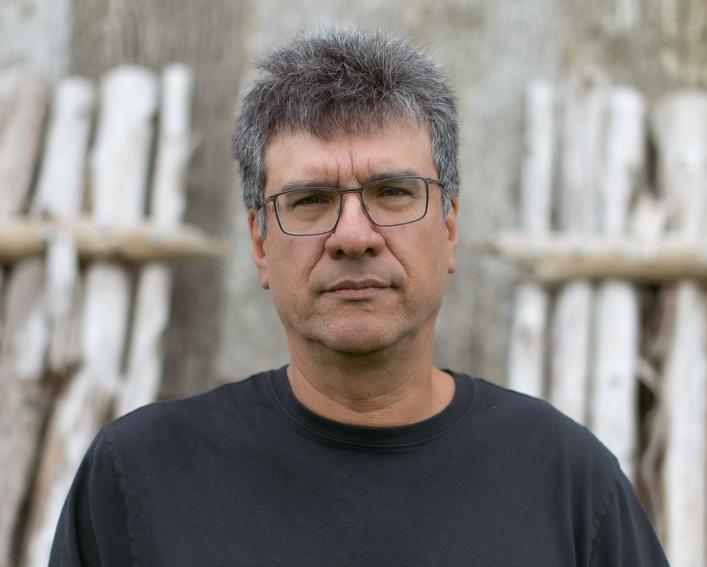 Photograph of a man with short dark grey hair wearing glasses and a black t shirt.