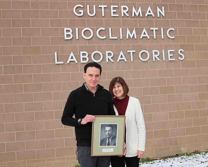 A man and a woman holding an old photo in front of the Guterman Bioclimatic Lab