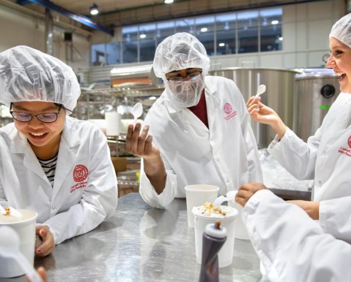 group of students in lab coats and hairnets tasting ice cream