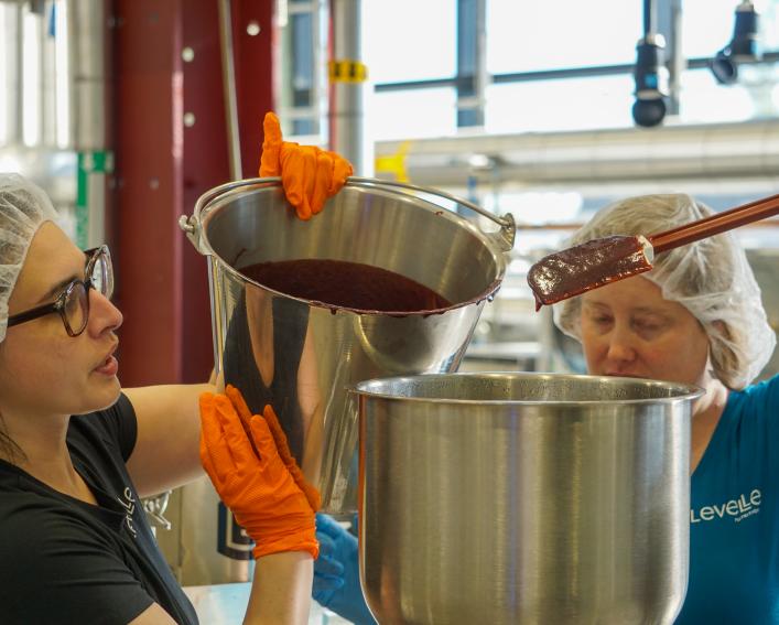 Linda Alvarez and Stephanie Schrauth pouring a bucket of fruit puree into another vessel. 