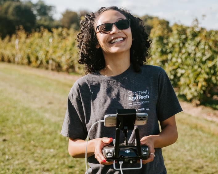 A woman wearing sunglasses uses a drone controller outside in a sunny field