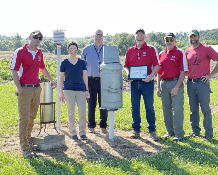 A group of people by are standing by a weather station with a certificate