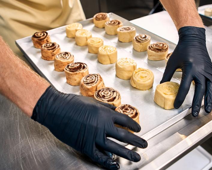 Worker wearing gloves handles pastries on a baking sheet
