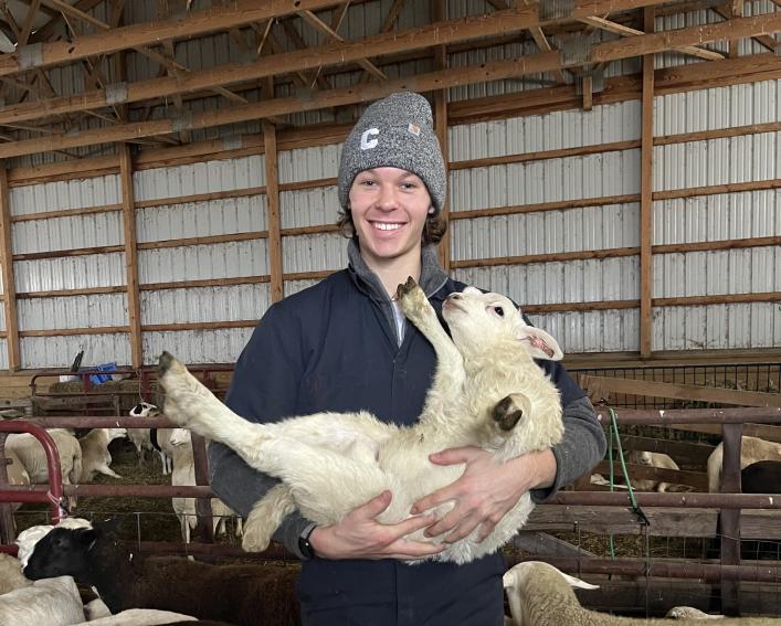 Alex holding a lamb in a barn. 