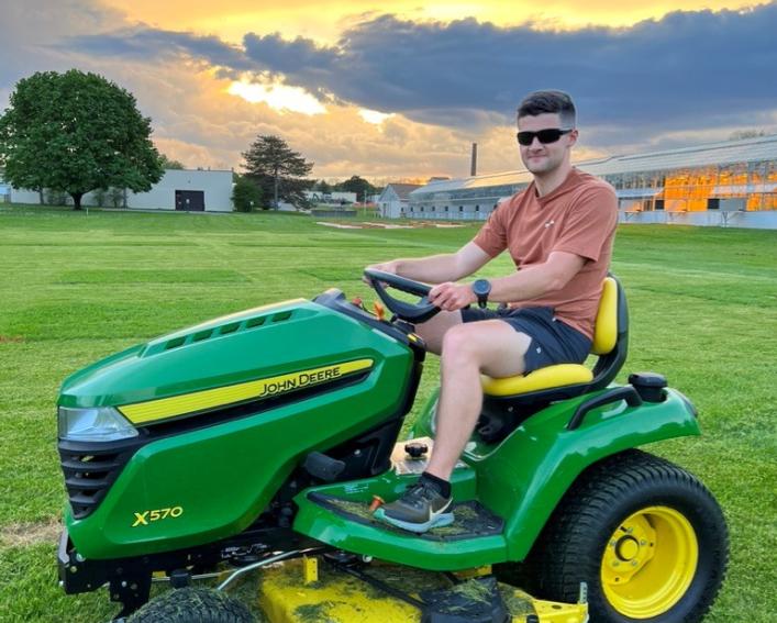 Hayden Bock rides a lawn mower at Cornell AgriTech.
