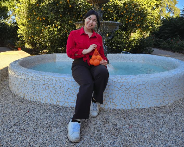 Sammi Lin sitting at a fountain holding a bag of orange 