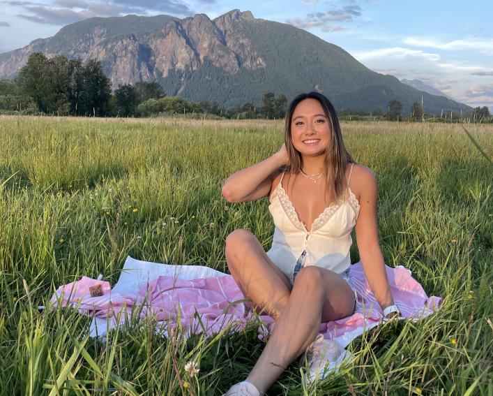 Sydney Wan sitting on a blanket in tall grass with mountains in the distance