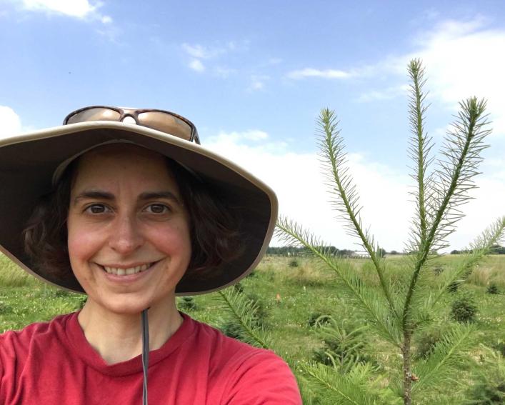 Person in a sun hat standing next to a Christmas tree