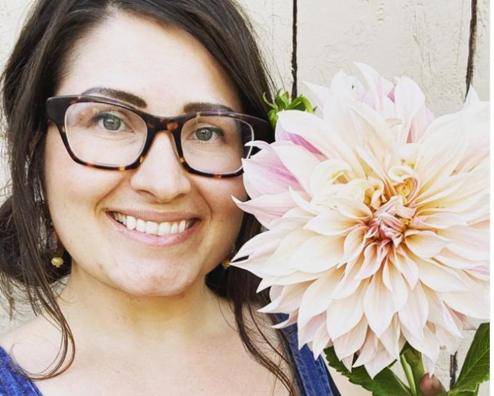 Person in overalls holding a huge flower and smiling