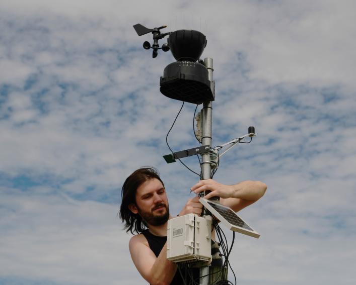person working on a weather station with clouds in the background