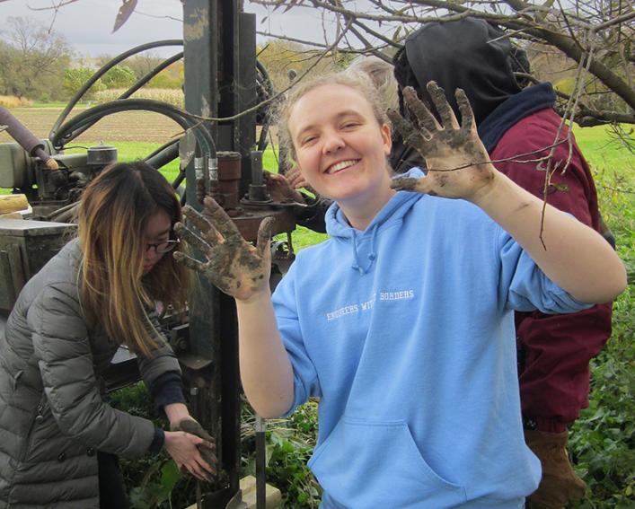 A student is showing off her dirty hands while working with equipment 