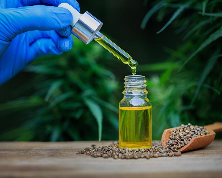 Hand drops oil into glass bottle in front of hemp plants